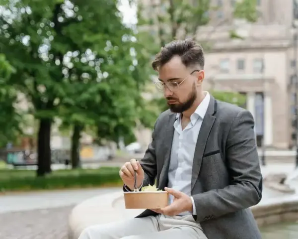 Mężczyzna w garniturze je sałatkę na zewnątrz.
