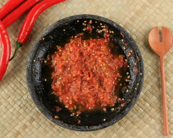 Świeżo przygotowany sos sambal w kamiennym moździerzu, obok czerwone papryczki chili i drewniana łyżka.