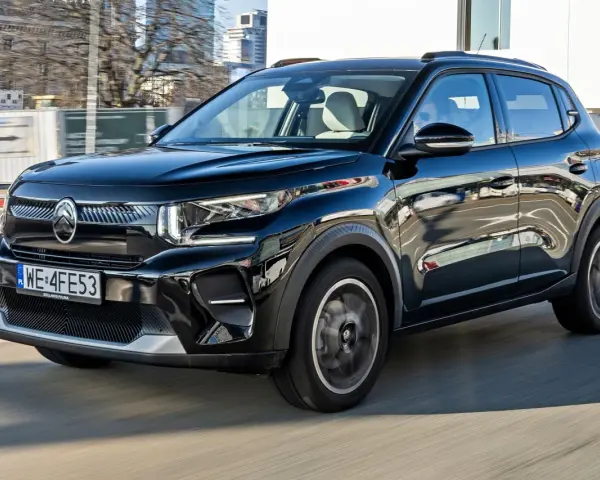 Czarny Citroen C3 porusza się po mieście, odbijając światła i budynki w swojej lśniącej karoserii.