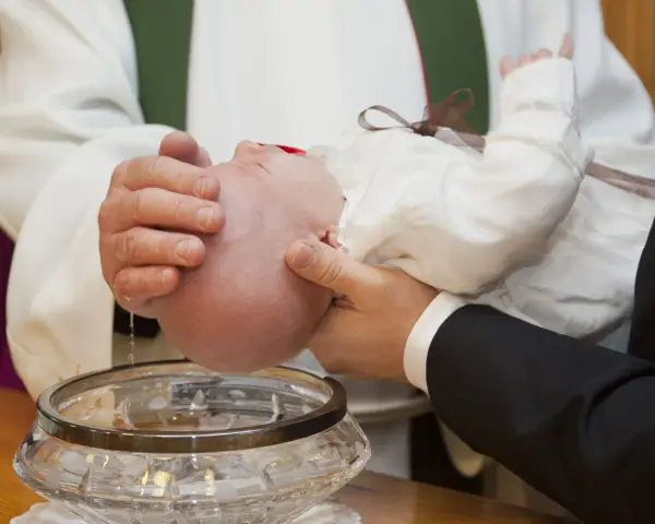 Chrzest chłopca: biała szatka, szklana chrzcielnica i woda święcona.
