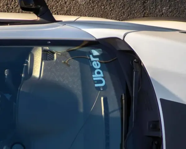 Fahrer hält das Lenkrad eines Autos mit Uber-Aufkleber auf der Windschutzscheibe.