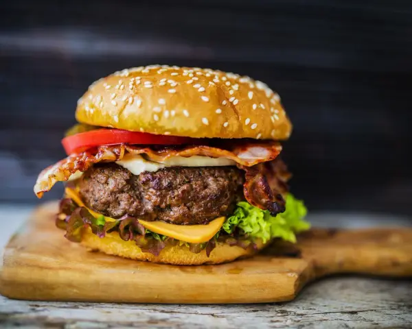 Soczysty burger z bekonem, serem, pomidorem i sałatą na desce.