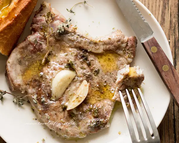 Succulenta braciola di maiale cotta con aglio e erbe aromatiche, servita con pane croccante.