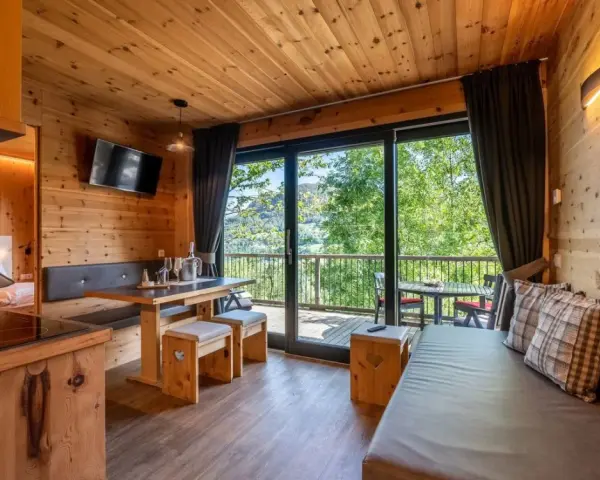 Przytulny domek z widokiem na góry, idealny na camping Seiser Alm. Drewniane wnętrze, wygodna kanapa i stół zapraszają do relaksu.