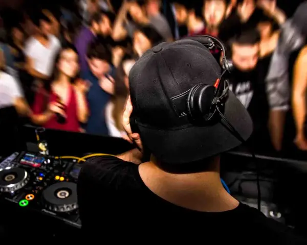 DJ aux platines, casque sur les oreilles, gérant le niveau sonore pour une foule en délire.