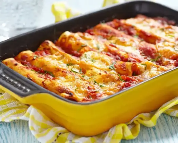 Pyszne cannelloni z mięsem mielonym, zapieczone pod sosem pomidorowym i serem, w żółtym naczyniu.