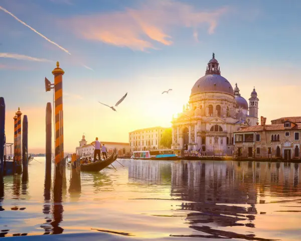 Gondola che scivola sull'acqua al tramonto, con la Basilica di Santa Maria della Salute sullo sfondo. Un'indimenticabile attività a Venezia.