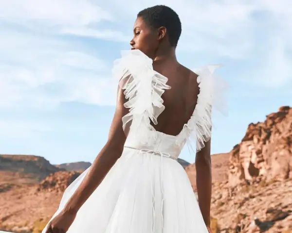 Novia con vestido blanco vaporoso, con volantes en los hombros, ideal para vestidos novia ibiza. Paisaje desértico al atardecer.