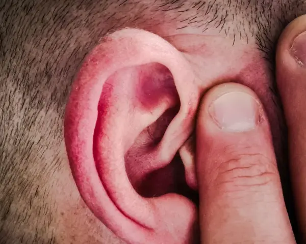 Un doigt pince l'oreille d'un homme, comme pour mieux capter un son aigu.