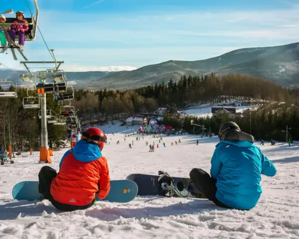 Dwaj snowboardziści odpoczywają na stoku, w tle widać wyciąg narciarski Karpacz i góry.