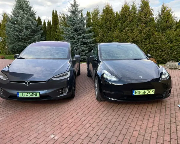 Dwa samochody Tesla, jeden ciemnoszary Model X, drugi czarny Model Y, stoją na podjeździe.