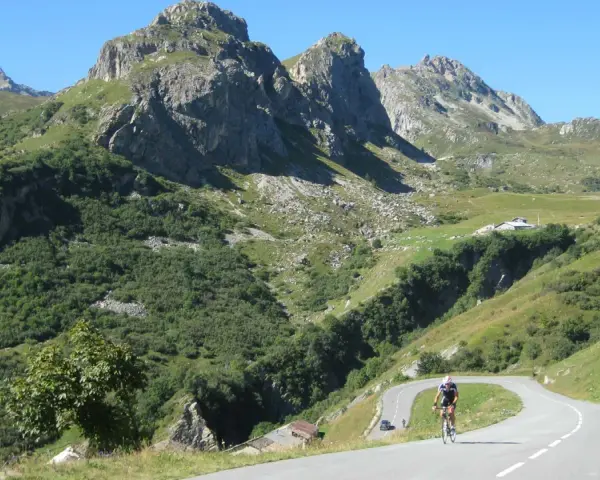 Ciclista su strada tortuosa verso il Cormet de Roselend, con montagne imponenti e verdi pendii.