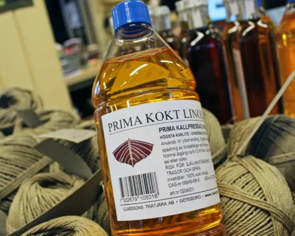 En flaska Prima kokt linolja, perfekt för fernissa oljemålning och ytbehandling av trä. Bredvid ligger härvor av garn.