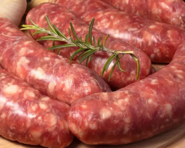 Salsiccia co to? Surowe kiełbaski wieprzowe, przyprawione ziołami, leżą na desce.