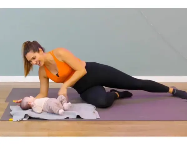 Une femme fait du sport après accouchement, en position de planche latérale, avec son bébé à ses côtés.