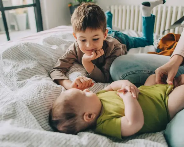 Starszy brat patrzy z czułością na niemowlę. Zastanawiamy się, ile cm rośnie dziecko w ciągu roku, obserwując te małe nóżki.