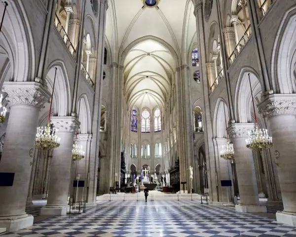 Wnętrze katedry Notre Dame, z monumentalnymi kolumnami, sklepieniem i witrażami. Na środku nawy stoi samotna postać.