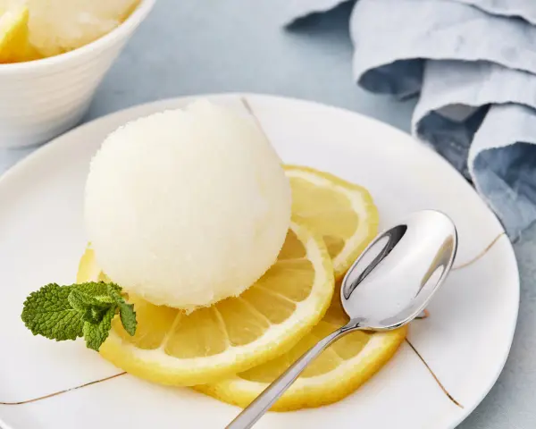 Erfrischendes Zitronensorbetto-Rezept: Eine Kugel Sorbet auf Zitronenscheiben mit Minze und Löffel.
