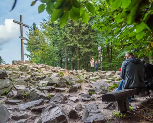 Kamieniste szlaki Gór Świętokrzyskich prowadzą do krzyża na szczycie. Ludzie odpoczywają na ławkach, podziwiając widoki.