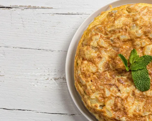 Frittata di cipolle dorata e soffice, guarnita con foglie di menta fresca, su un piatto bianco appoggiato su un tavolo di legno sbiancato.