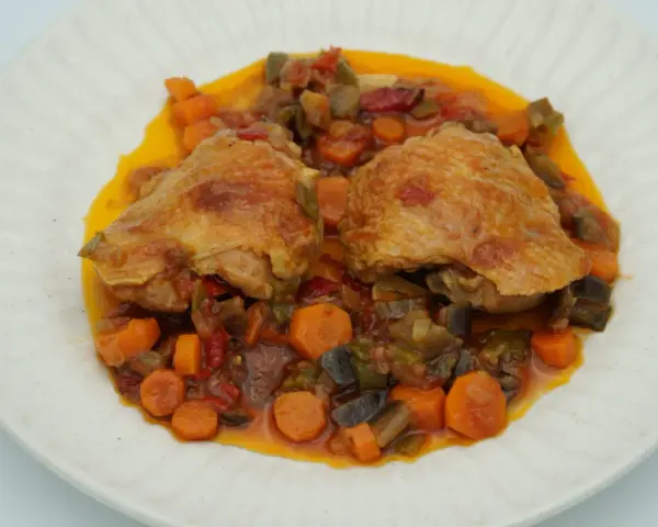 Dos piezas de pollo dorado sobre un guiso de verduras coloridas, zanahorias y berenjenas. Un delicioso pollo a la jardinera.