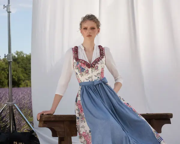 Ein Dirndl im floralen Muster mit blauem Rock, ein moderner Dirndl-Trend, posiert vor Lavendelfeld-Kulisse.