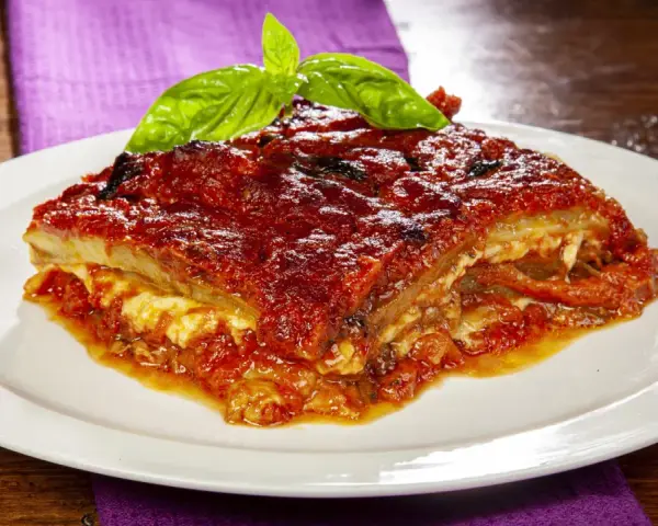 Una fetta di parmigiana di melanzane napoletana, ricca e saporita, guarnita con basilico fresco.