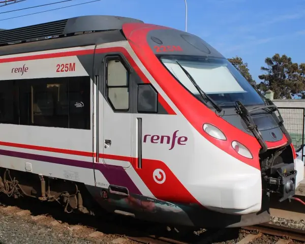 Czoło pociągu Renfe 225M z czerwonymi i białymi pasami, stojącego na torach.