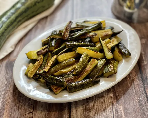 Zucchine al forno dorate e saporite, tagliate a bastoncini e servite su un piatto bianco.