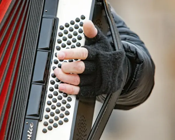 Dłoń w rękawiczce gra na akordeonie, wydobywając dźwięki tego wyjątkowego instrumentu.