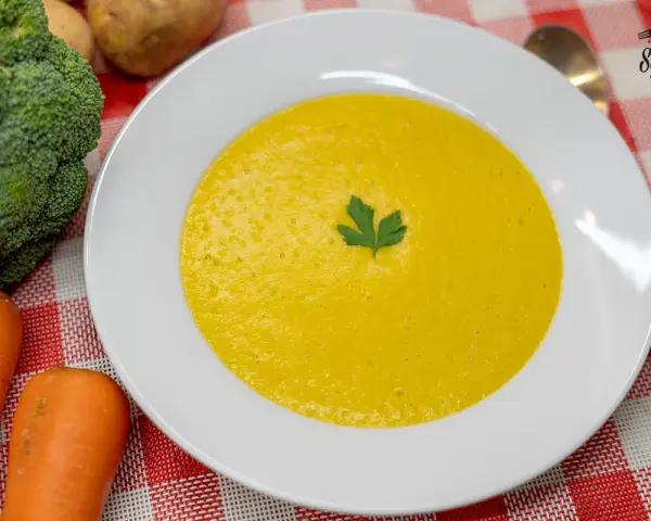 Un cremoso puré de verduras, con brócoli y zanahorias frescos al lado, listo para disfrutar.