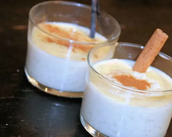 Deux verres de riz au lait crémeux, saupoudrés de cannelle. Un bâton de cannelle décore l'un des desserts, parfait pour une recette de riz au lait.