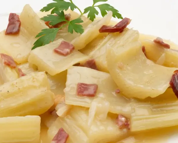 Cardo a la navarra, un plato tradicional con trozos tiernos de cardo en una cremosa salsa, adornado con trocitos de jamón y perejil fresco.
