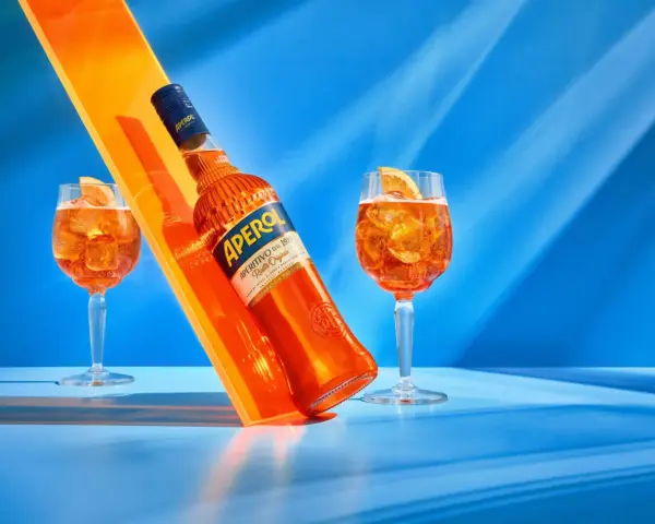 Aperol, znany z orzeźwiającego smaku, ma 11% alkoholu. Na zdjęciu butelka i dwa drinki z pomarańczą.