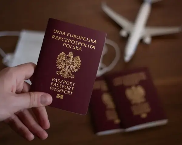 Dłoń trzyma polski paszport. Obok leżą kolejne paszporty, maseczka i samolot. Zastanawiasz się, ile się czeka na paszport?