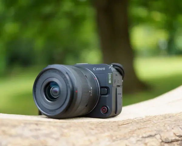 Un appareil photo Canon EOS R50, prêt pour un test en extérieur. Le soleil brille sur son objectif.