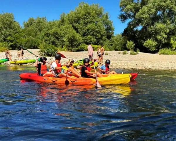 Des personnes profitent d'une activité canoe kayak sur une rivière ensoleillée, entourées de verdure et d'une plage de galets.