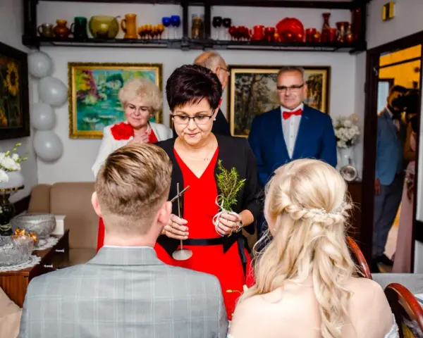 Tradycyjne błogosławieństwo pary młodej. Kobieta w czerwonej sukience trzyma gałązkę ziół, błogosławiąc narzeczonych.