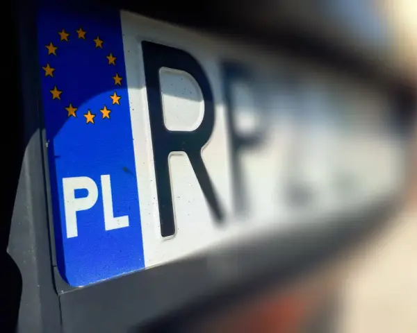 Zbliżenie na polską tablicę rejestracyjną z symbolem UE. Litery "PL" i fragment innych znaków sugerują, że pojazd jest w trakcie wyrejestrowania.