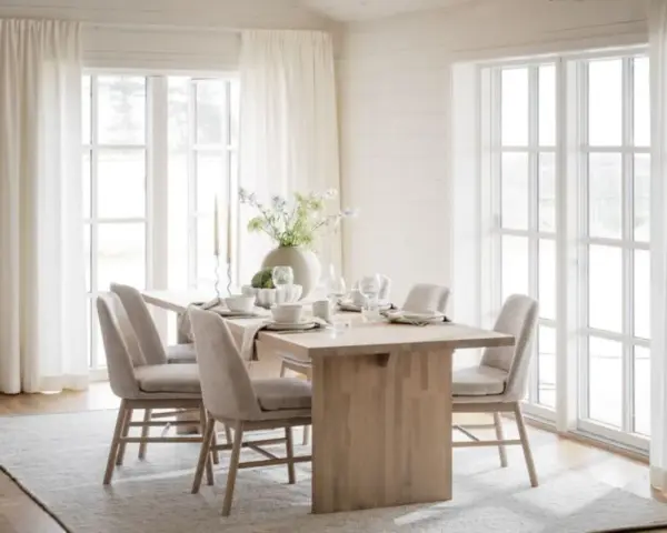 Ljust och luftigt kök med ett träbord dukat för middag. Inspiration dekoration matbord med en stor vas med blommor och ljus.