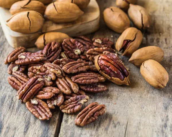 Noix de pécan décortiquées et entières sur fond de bois. Découvrez le noix de pécan bienfait pour une alimentation saine et gourmande.