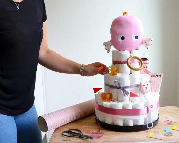 En person lägger sista handen vid en blöjtårta dekoration med en rosa bläckfisk som topp.