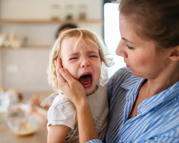 Mama próbuje uspokoić płaczące dziecko, które przeżywa histerię. 5-latek krzyczy, a mama delikatnie trzyma go za policzek.
