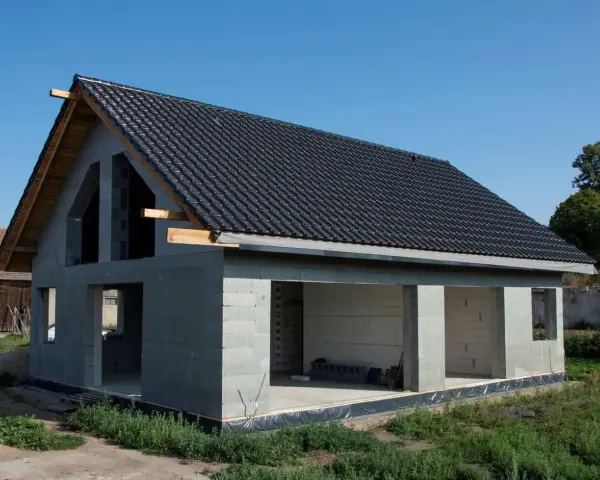 Dom w stanie surowym w Poznaniu, z czarnym dachem i szarymi ścianami z bloczków.