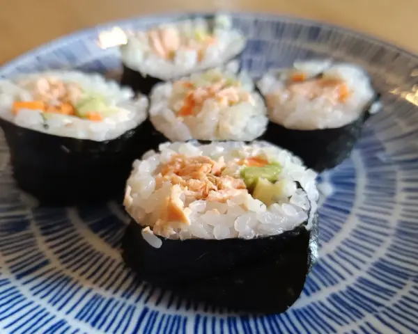 Pięć kawałków sushi z łososiem, ryżem i warzywami na niebiesko-białym talerzu.
