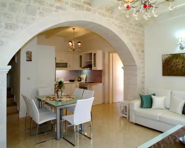 Un elegante soggiorno con un **arco in pietra moderno** che separa la zona pranzo dalla cucina. Divano bianco, quadri e lampadario di cristallo.