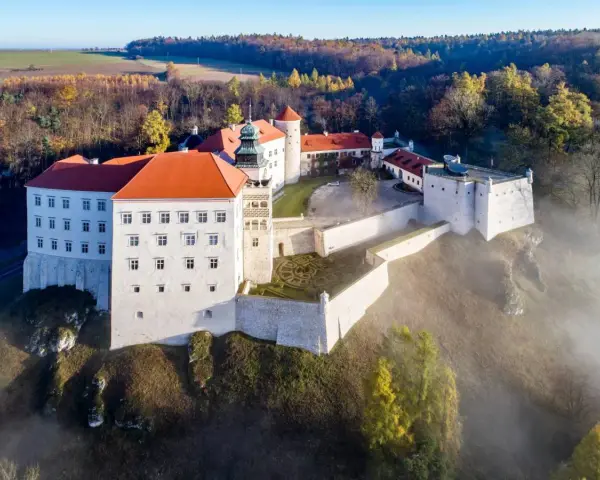 Majestatyczny zamek pod Krakowem, otoczony mgłą i jesiennym lasem, wznosi się na wzgórzu.