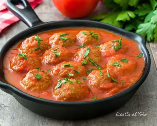 Polpette di lenticchie in salsa di pomodoro, guarnite con prezzemolo fresco, servite in una padella nera su un tavolo di legno.