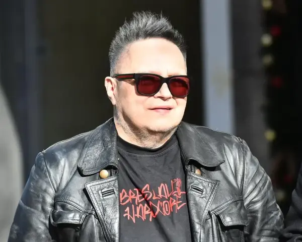Charyzmatyczny wokalista w skórzanej kurtce i okularach przeciwsłonecznych, z charakterystyczną fryzurą.