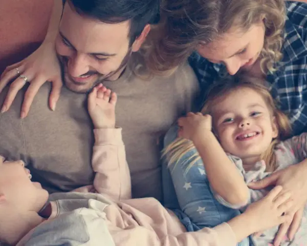 Glückliche Familie kuschelt auf dem Sofa. Zwei Elternteile umarmen ihre zwei Kinder, die sich an sie schmiegen.